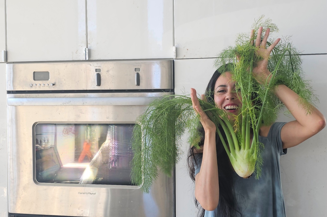 Cheryl Devine plant-based holistic nutritionist smiling holding up a huge fennel by her oven and pantry